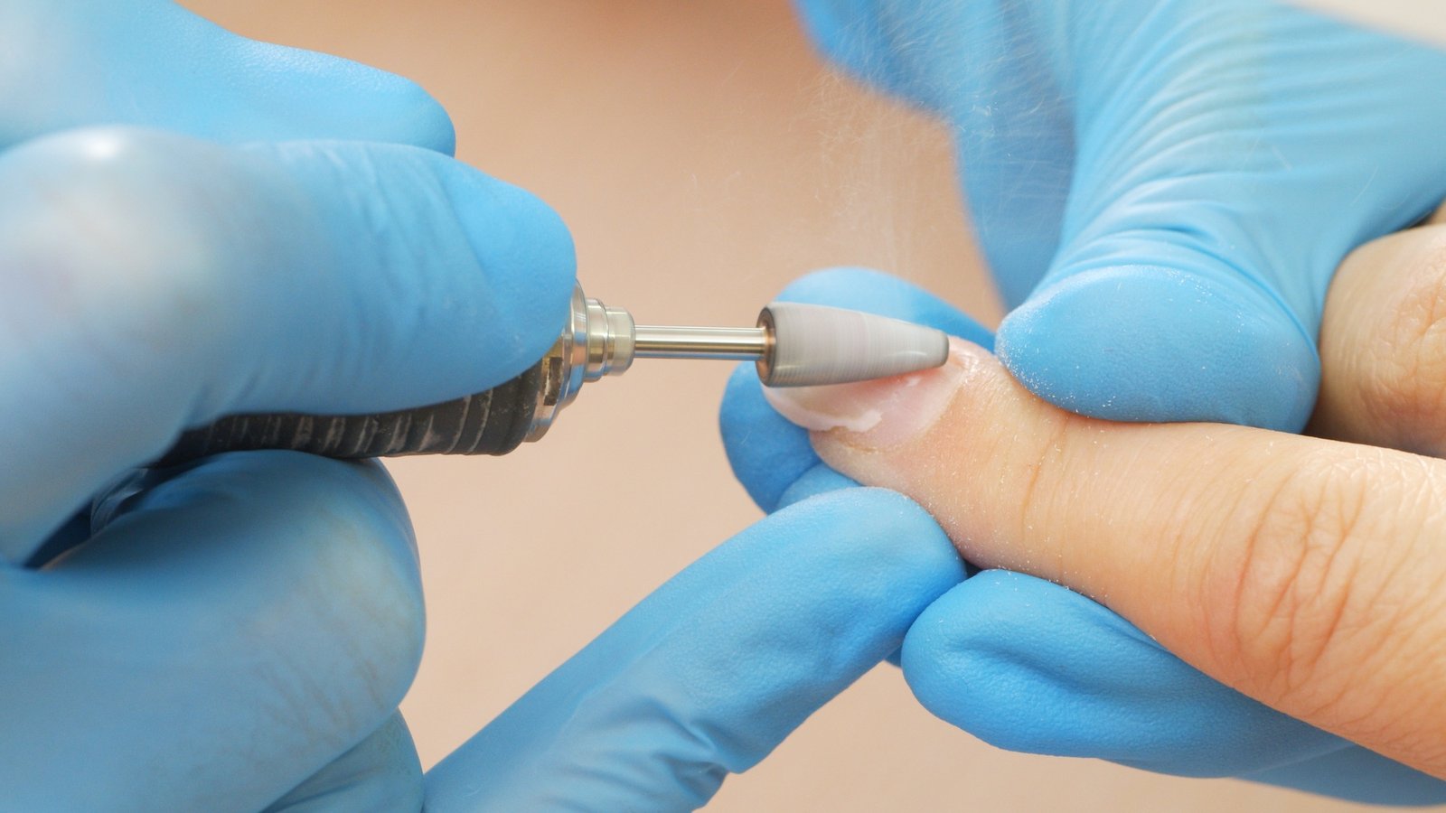 Manicurist in process of removing gel polish or acrylic from nails using manicure machine.